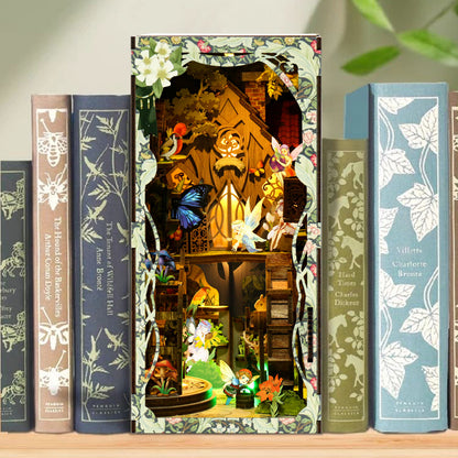 A miniature forest scene with a fairy house, flowers, and various woodland creatures is displayed on a bookshelf among other books.