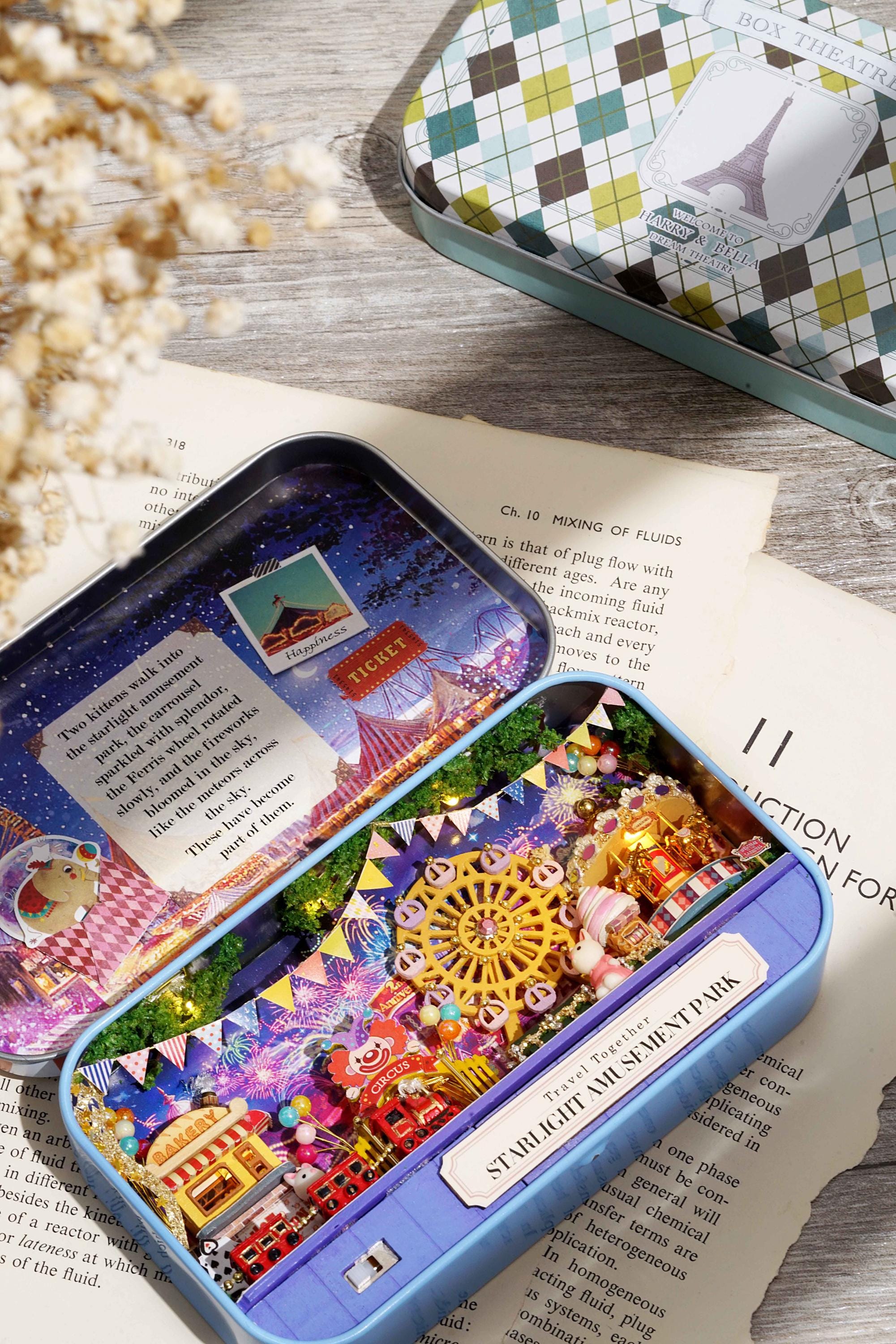 Mini amusement park diorama tin open on a book, showing illuminated fairground scene