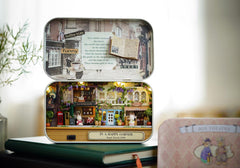 Box theater diorama display on table with lid open, and a pink fabric carry case beside it