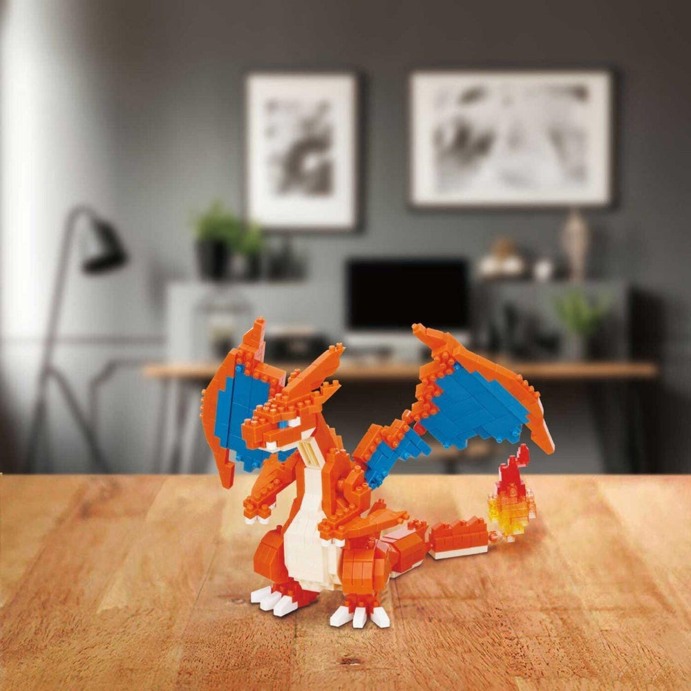 A LEGO Charizard figurine is displayed on a wooden surface, with a blurred background featuring a desk, plants, and artwork.