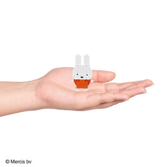 A small white rabbit figurine is being held in a person's hand against a white background.