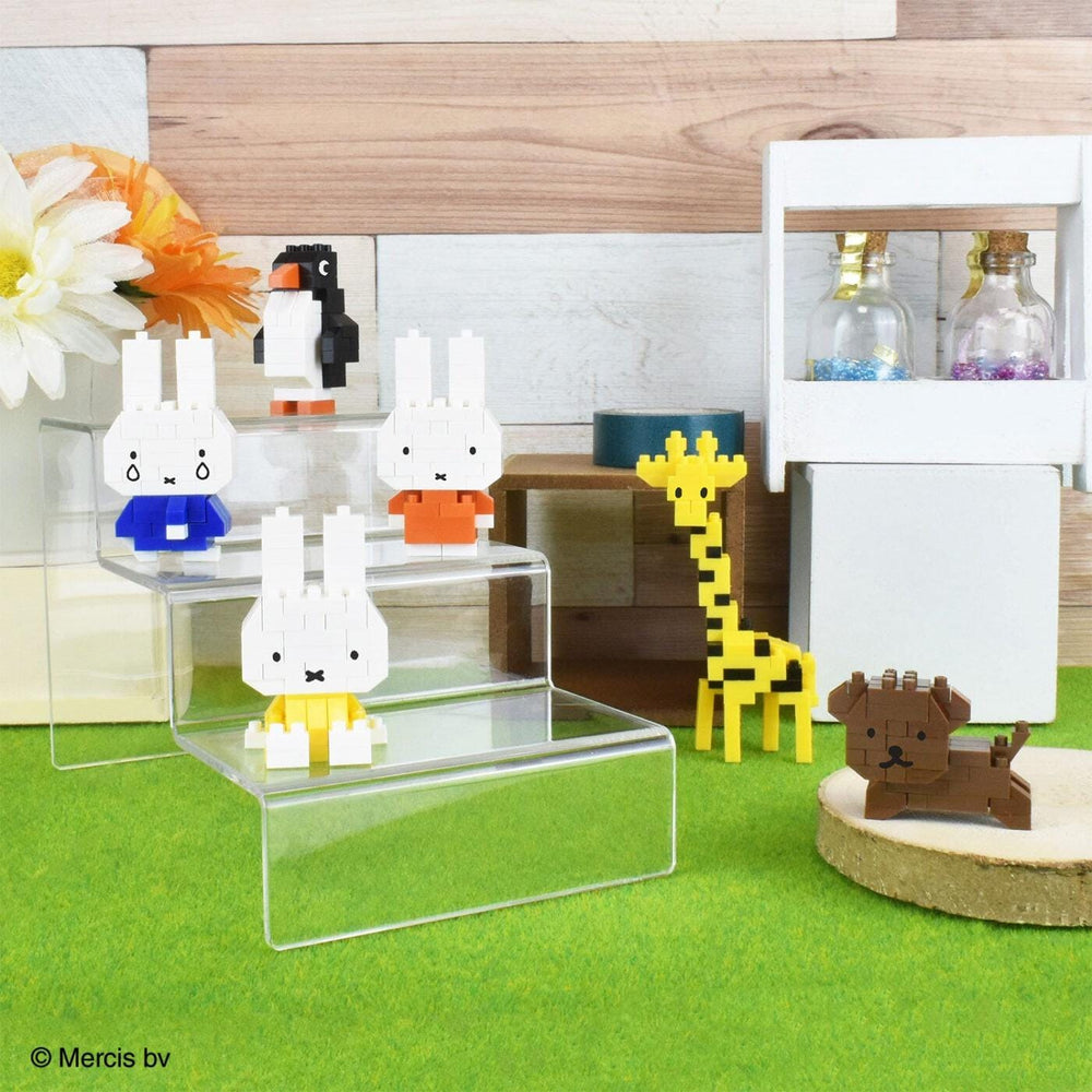 A collection of colorful, small toy figurines, including a penguin, rabbit, giraffe, and dog, arranged on a green surface.