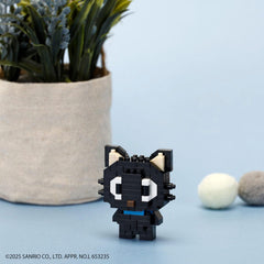 A small black cat-shaped figure made of small building blocks is sitting on a light blue surface, with a potted plant and two balls in the background.