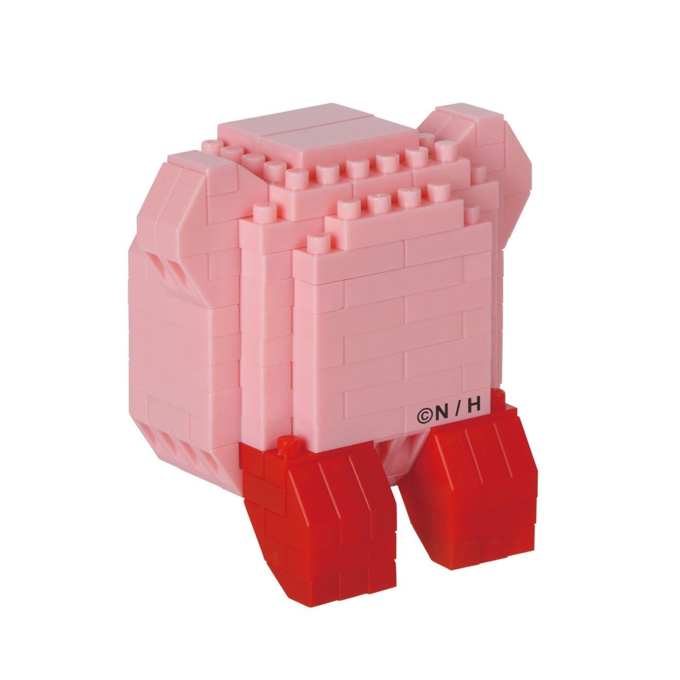 A pink, brick-like toy figure with red legs, sitting on a white background.