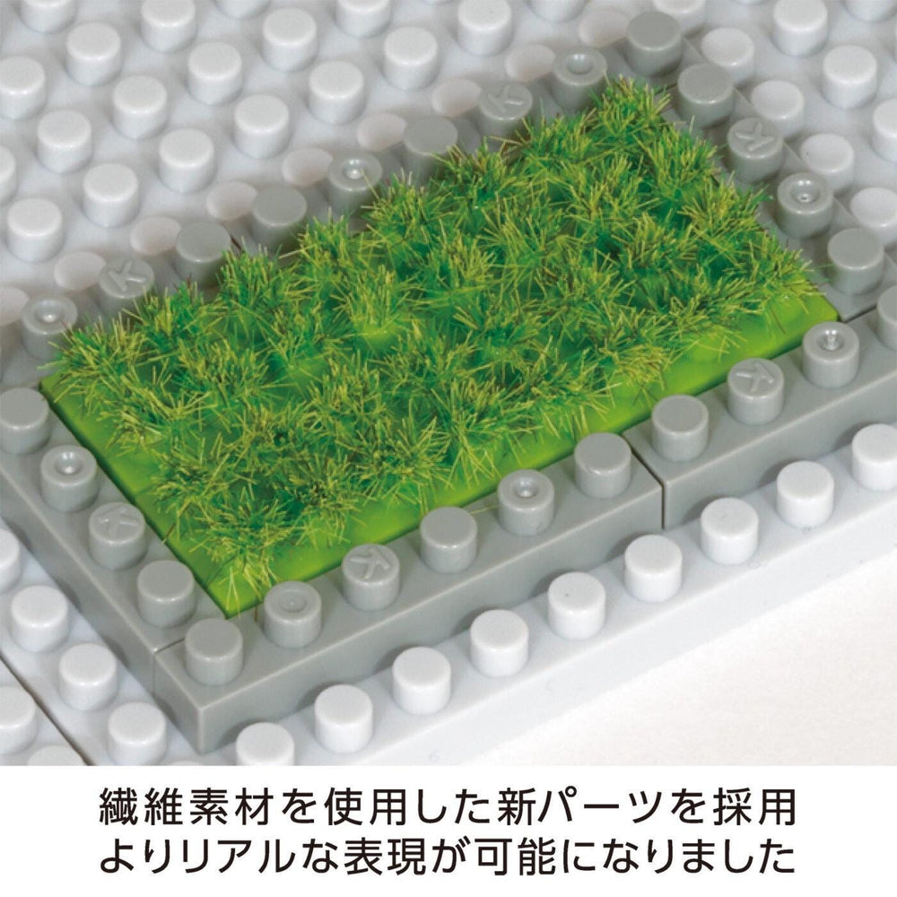 A close-up image of a green grass-like material placed on a white surface, surrounded by gray and white Lego bricks.