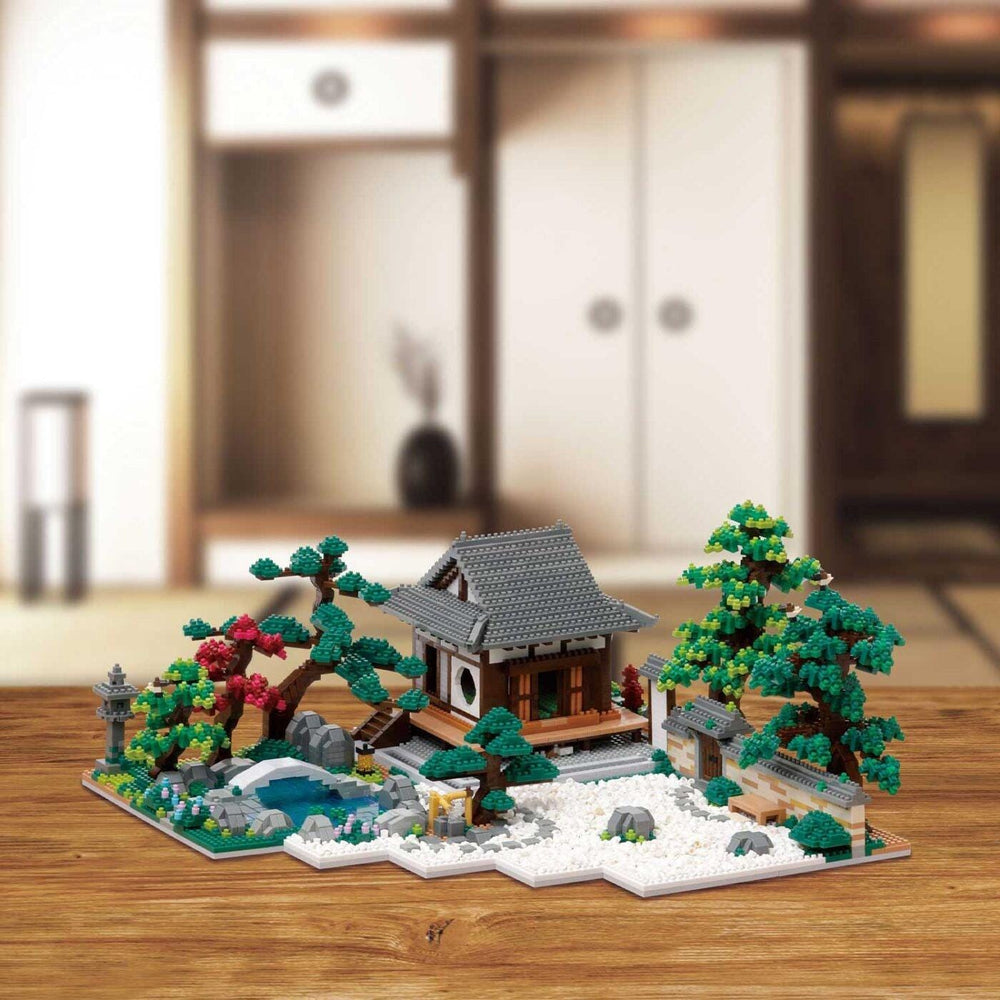 A miniature Japanese-style garden with a small wooden house, trees, and a pond, all crafted from building blocks.