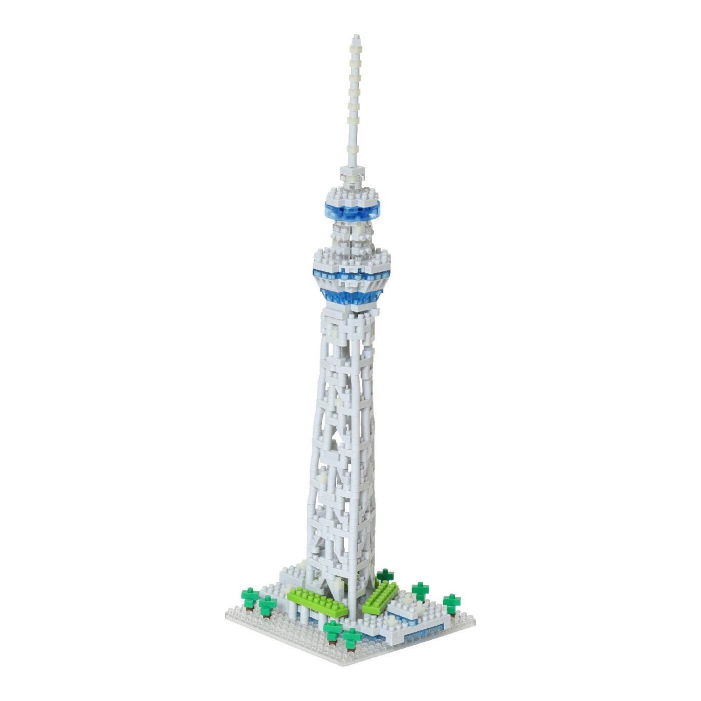 A white and blue Lego tower with a pointed spire, standing on a base with green trees.