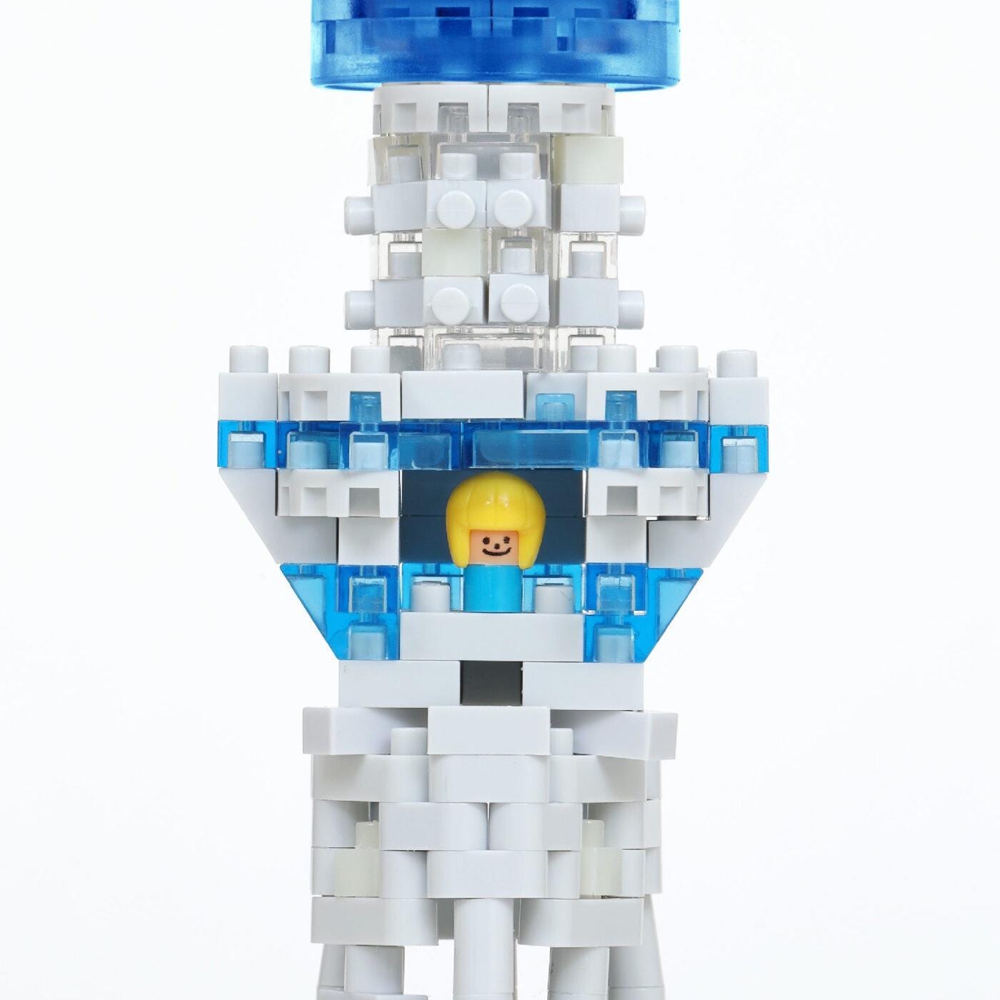 A close-up of a white and blue Lego structure with a yellow figure inside, set against a white background.