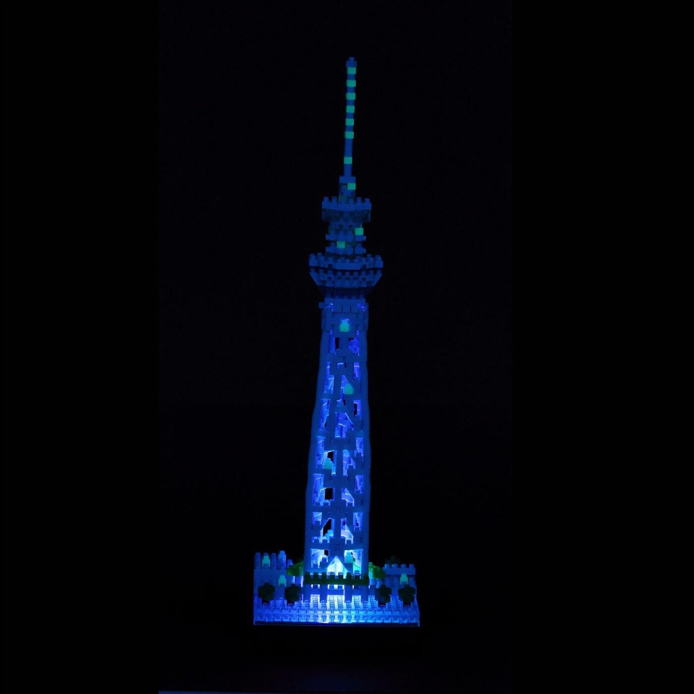 A blue and white illuminated model of the Tokyo Skytree, a famous landmark in Japan, stands prominently against a dark background.