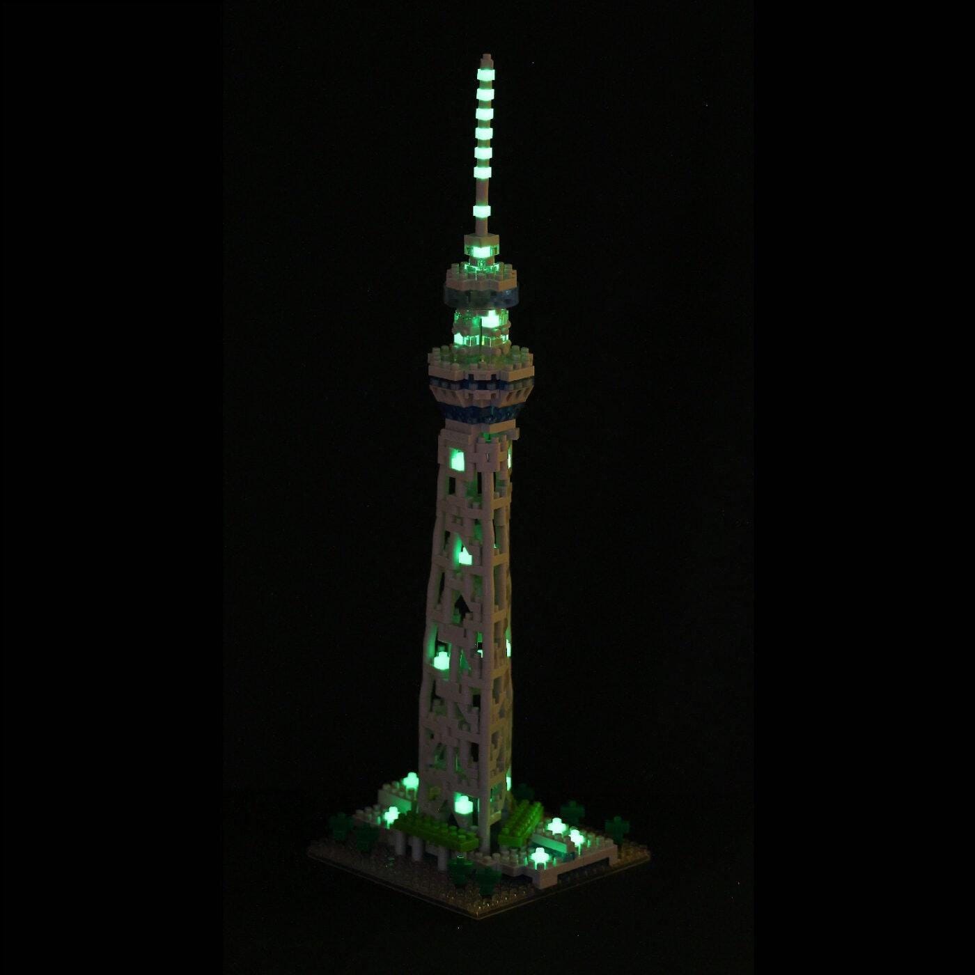 A tall, illuminated tower made of small, glowing blocks stands against a dark background.