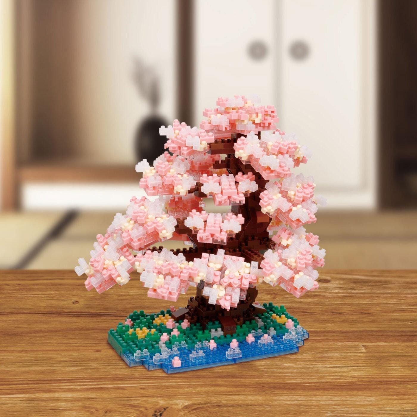 A pink and white miniature tree made of small building blocks is displayed on a wooden table.