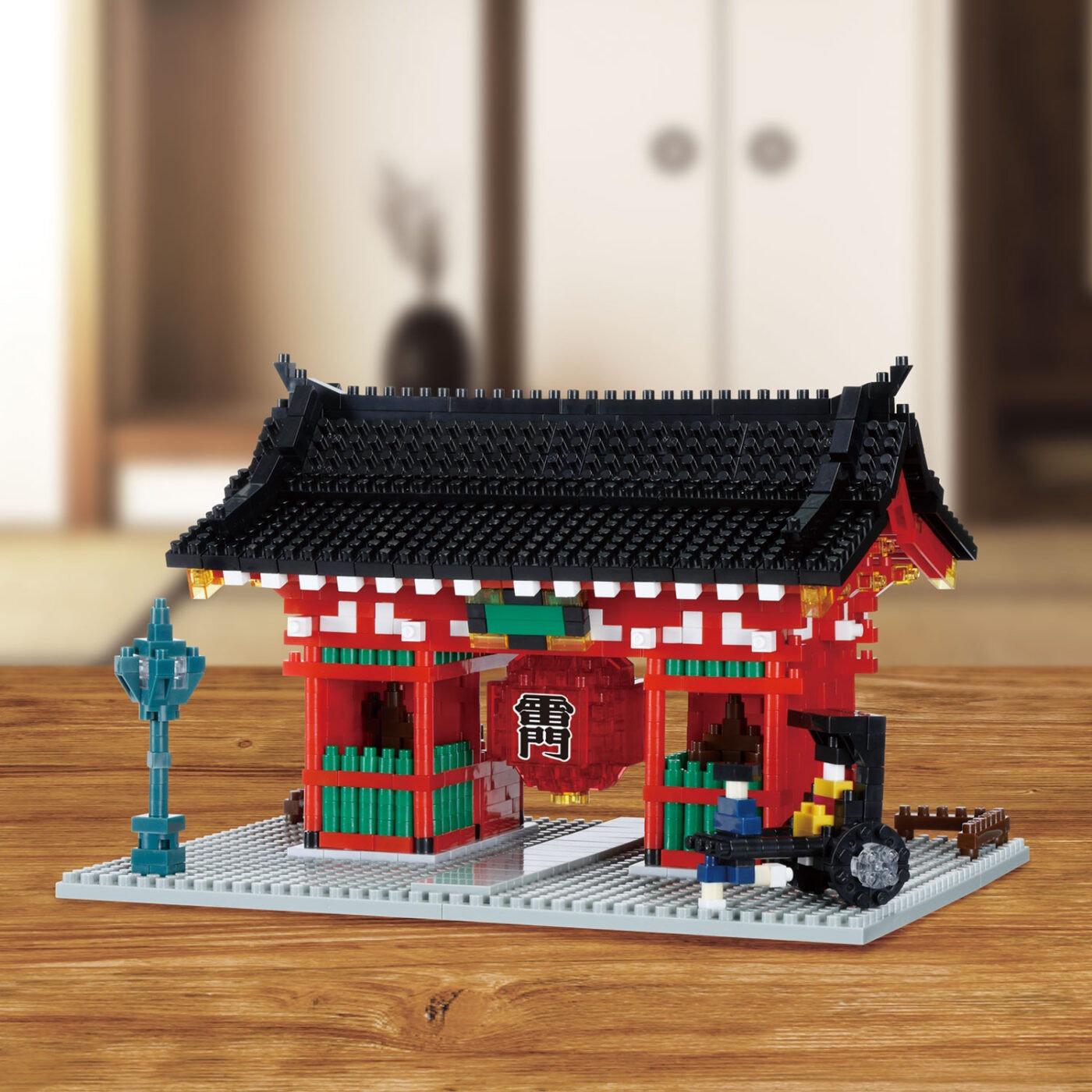 A colorful, intricately designed toy temple made of small building blocks, featuring a red roof, green and white accents, and a red lantern hanging from the center.