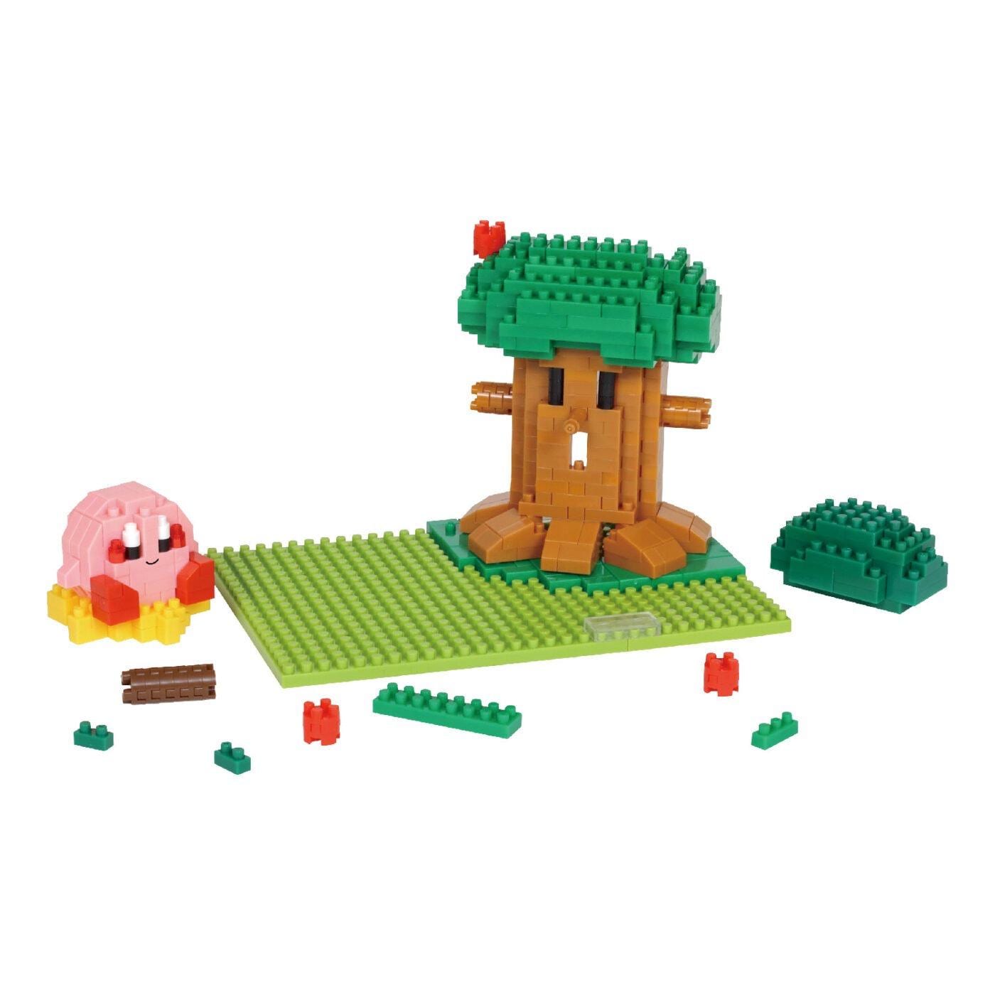 A colorful toy tree made of small building blocks, with a pink character sitting on the ground next to it. There are also some additional building block pieces scattered around the tree.