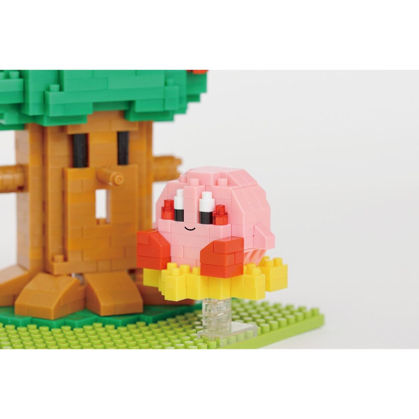 A pink and yellow pixelated character resembling a character from a video game, standing next to a green tree-like structure made of small building blocks.