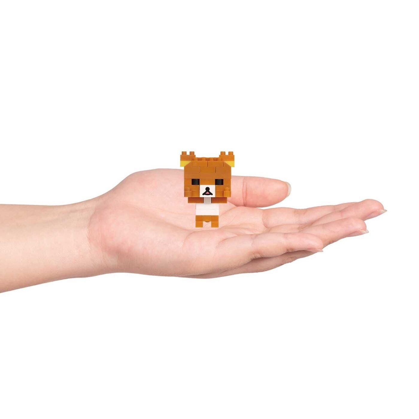 A small, pixelated brown bear figurine is being held in a person's hand against a white background.