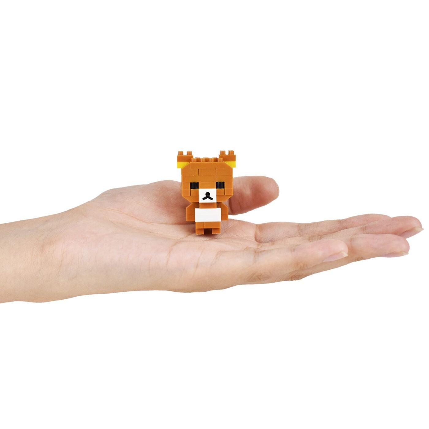 A small, pixelated brown bear figurine is being held in a person's hand against a white background.