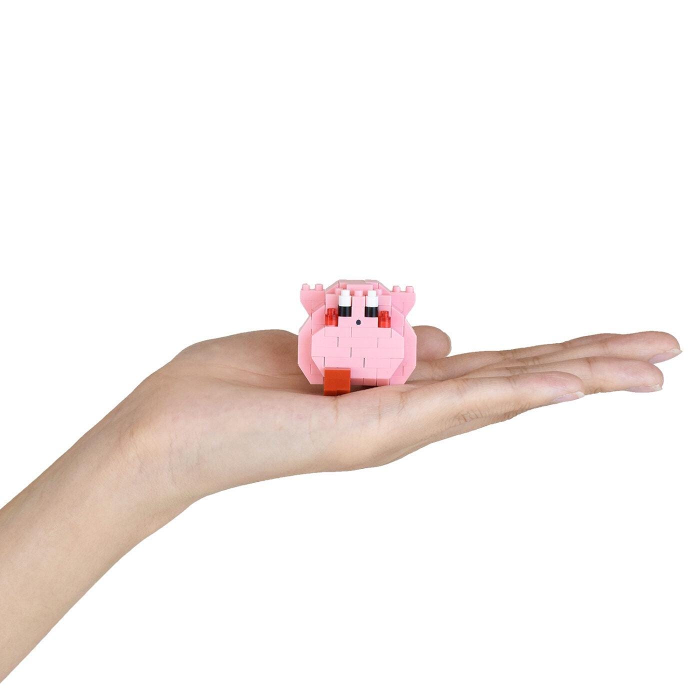 A hand holding a small pink, brick-like object with a face and eyes.