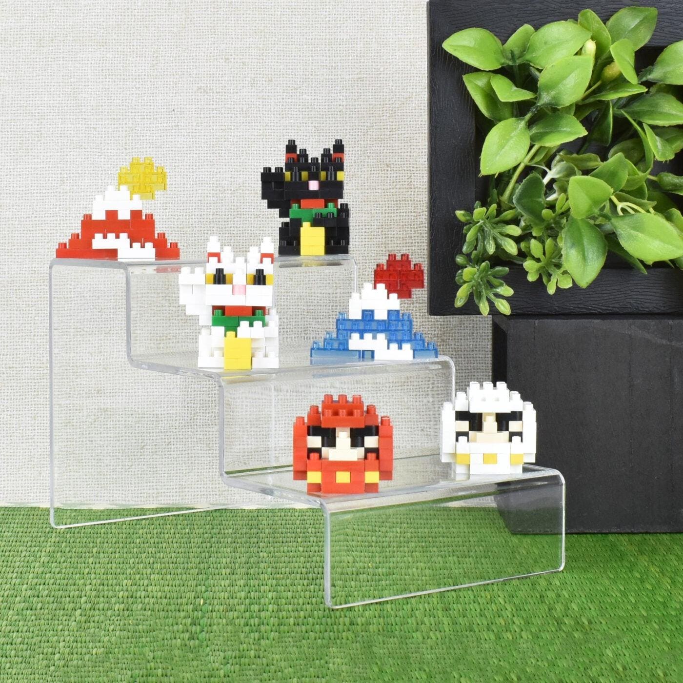 A display of colorful, pixelated character figurines on a clear, three-tiered stand, with a potted plant in the background.