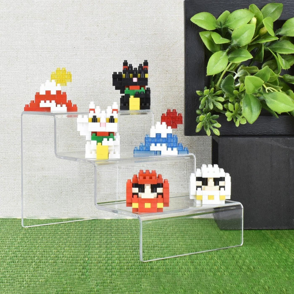 A display of colorful, pixelated character figurines on a clear, three-tiered stand, with a potted plant in the background.