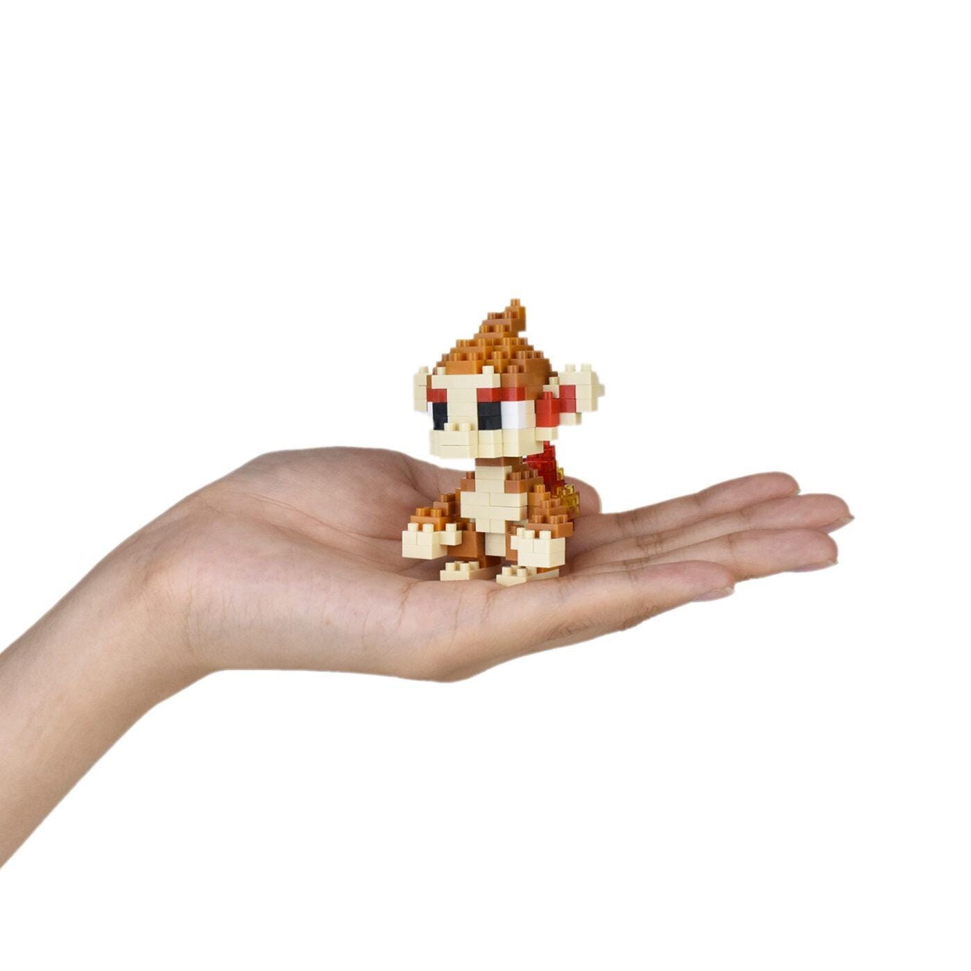 A small, pixelated monkey figurine is being held in a person's hand against a white background.
