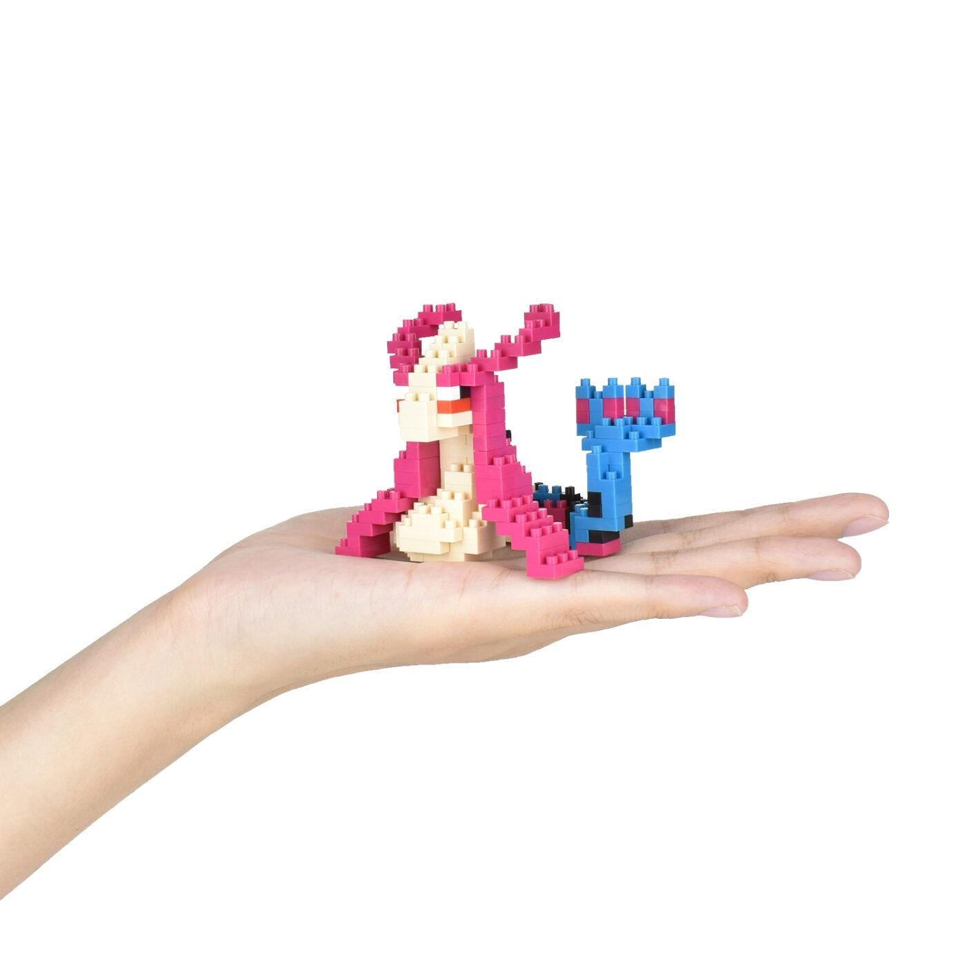 A hand holding a small, colorful, pixelated toy in the shape of a fish.