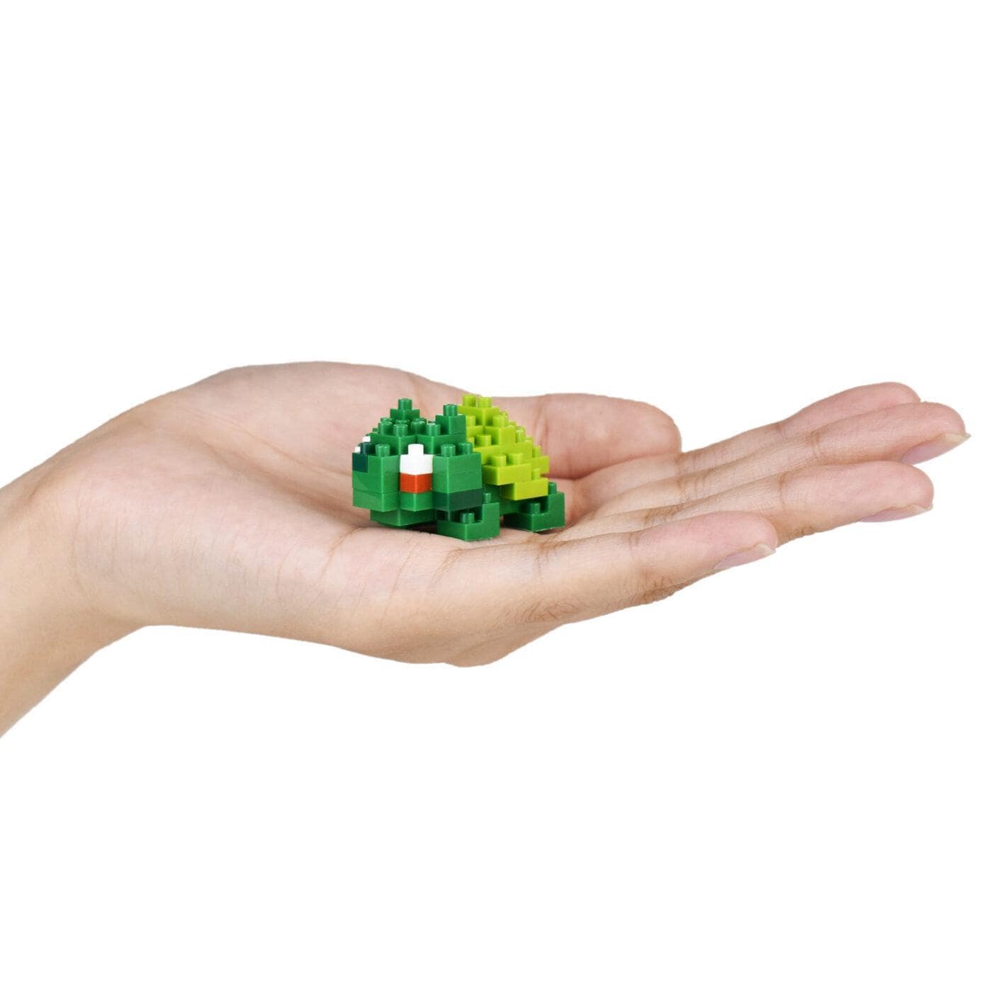 A hand holding a small green and white toy in the palm.