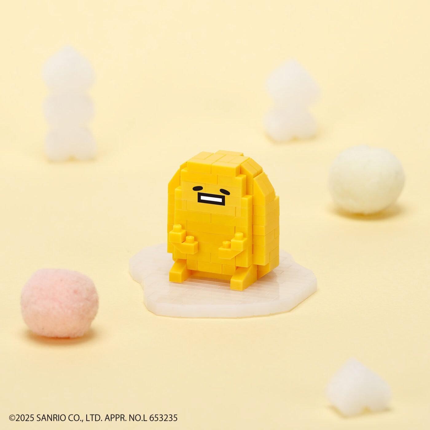 A yellow pixelated character resembling a yellow egg is surrounded by various objects, including a pink ball, a white ball, and a small white object, all set against a yellow background.