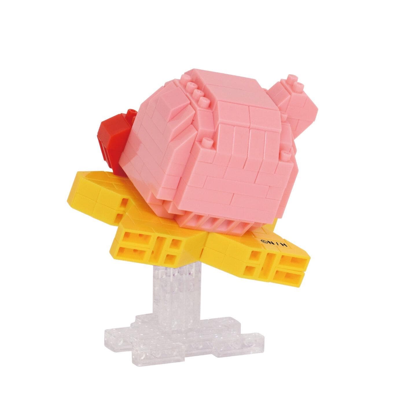 A pink and yellow toy figure, resembling a pink pig or a pink and yellow building, is shown on a clear stand.