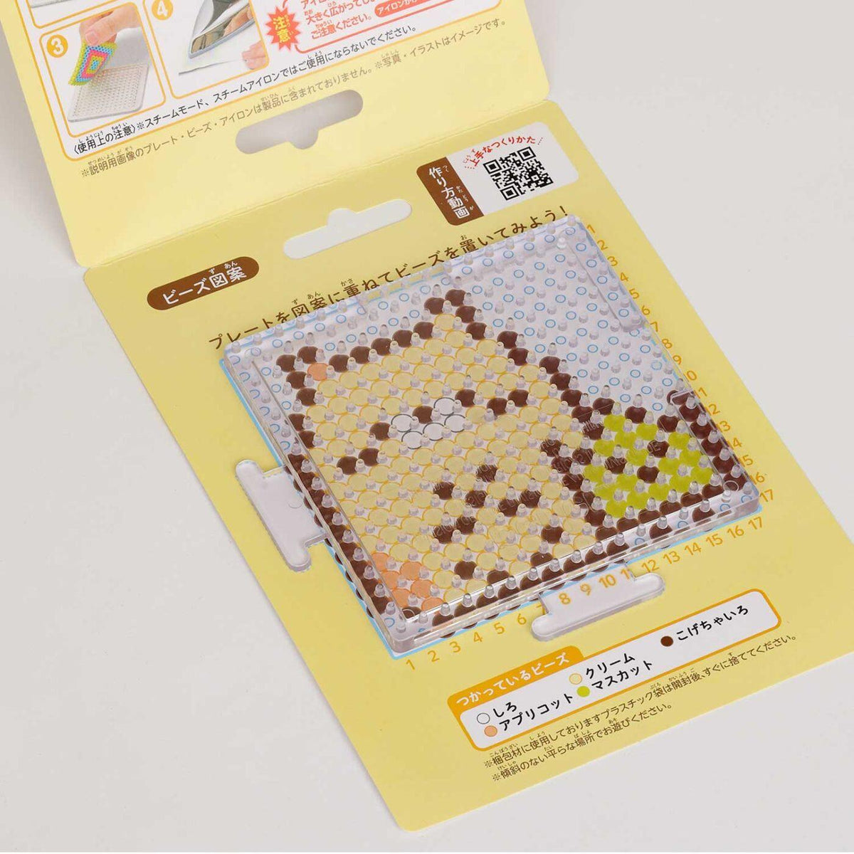 a yellow and white packaging for a product, likely a craft item or kit, with a clear plastic piece featuring a pixelated design.