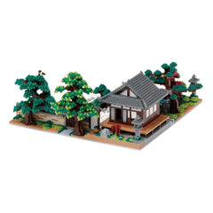 A detailed model of a Japanese-style house with a tiled roof, surrounded by trees and other miniature elements, such as a stone lantern and a small pond.