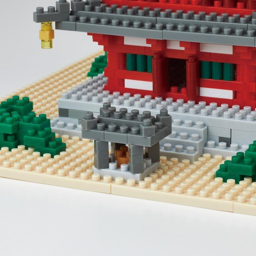 A close-up view of a toy model of a temple made of small building blocks, with a red and white exterior and green accents.