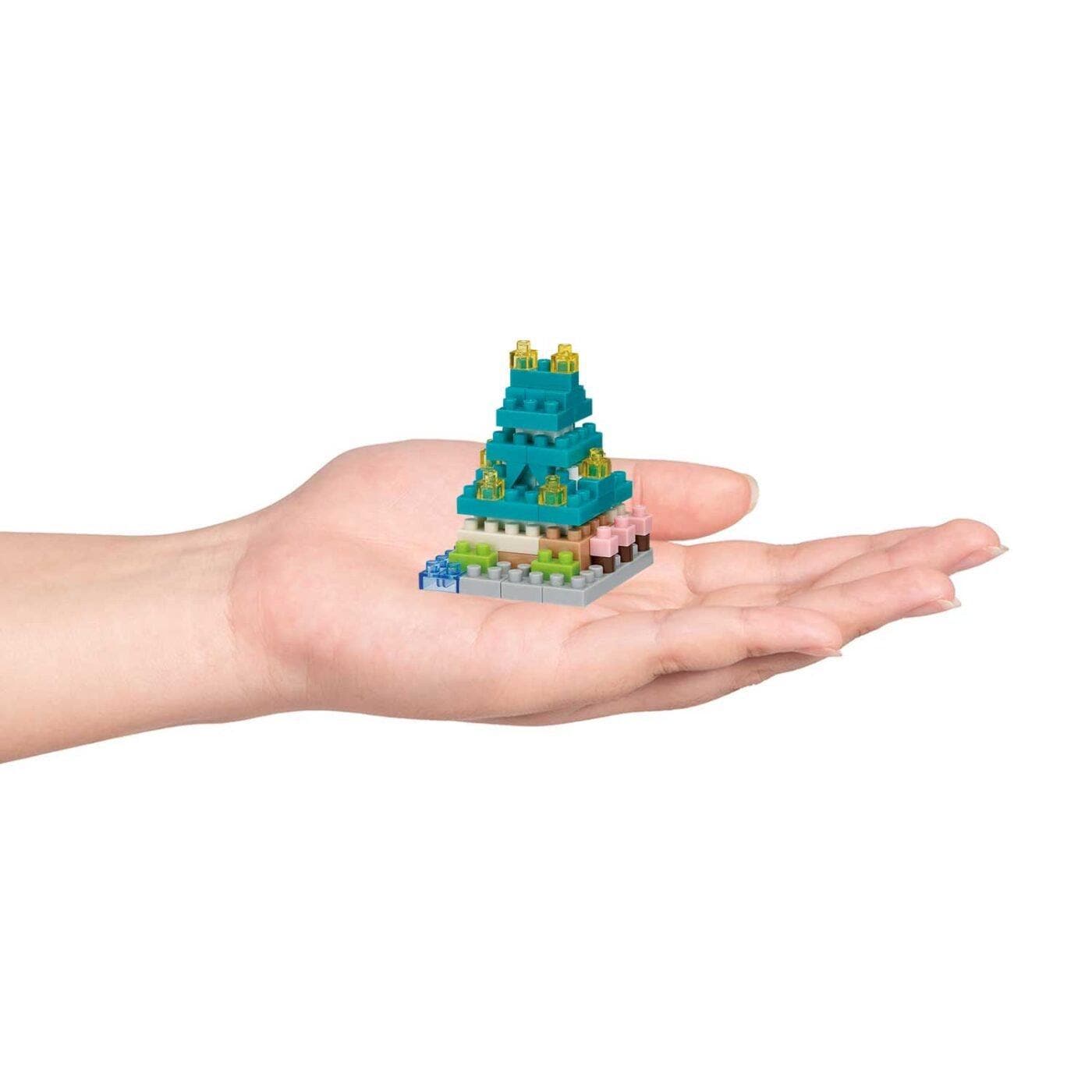 A hand holding a small, colorful, and intricate toy or model, resembling a miniature version of a larger structure or object.