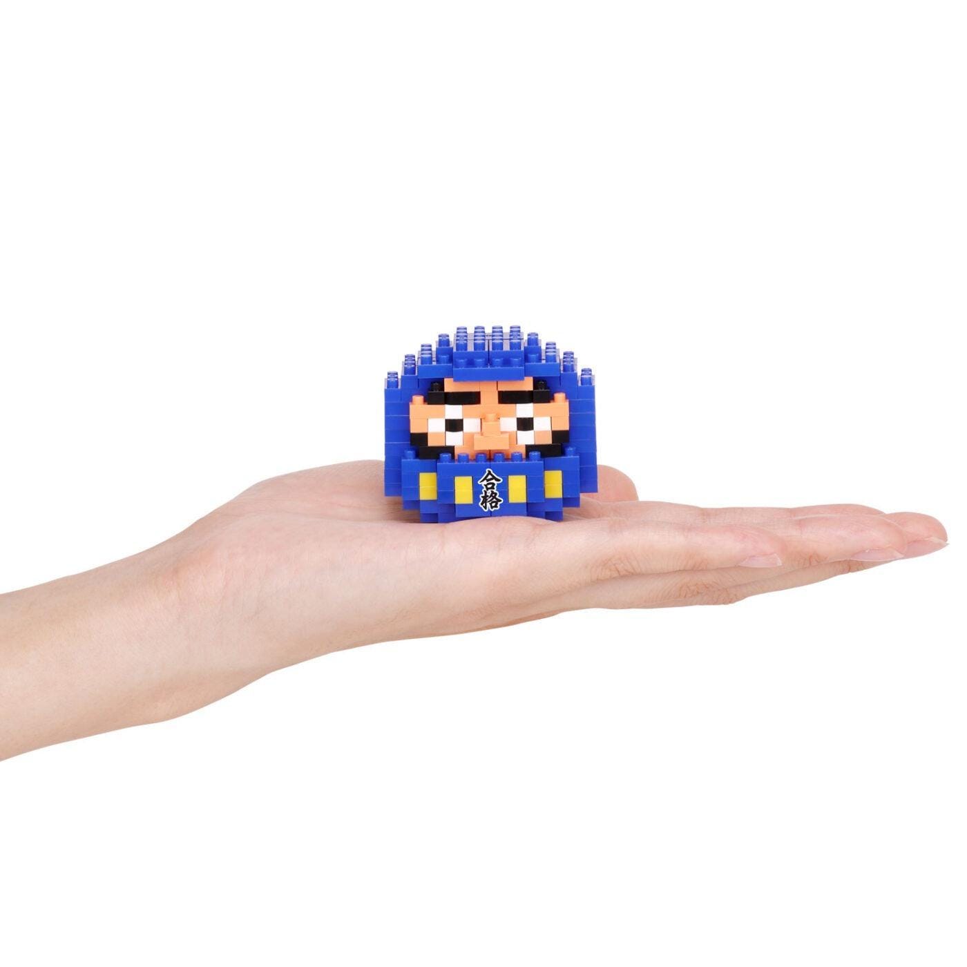 A hand holding a small blue and yellow pixelated character or toy.