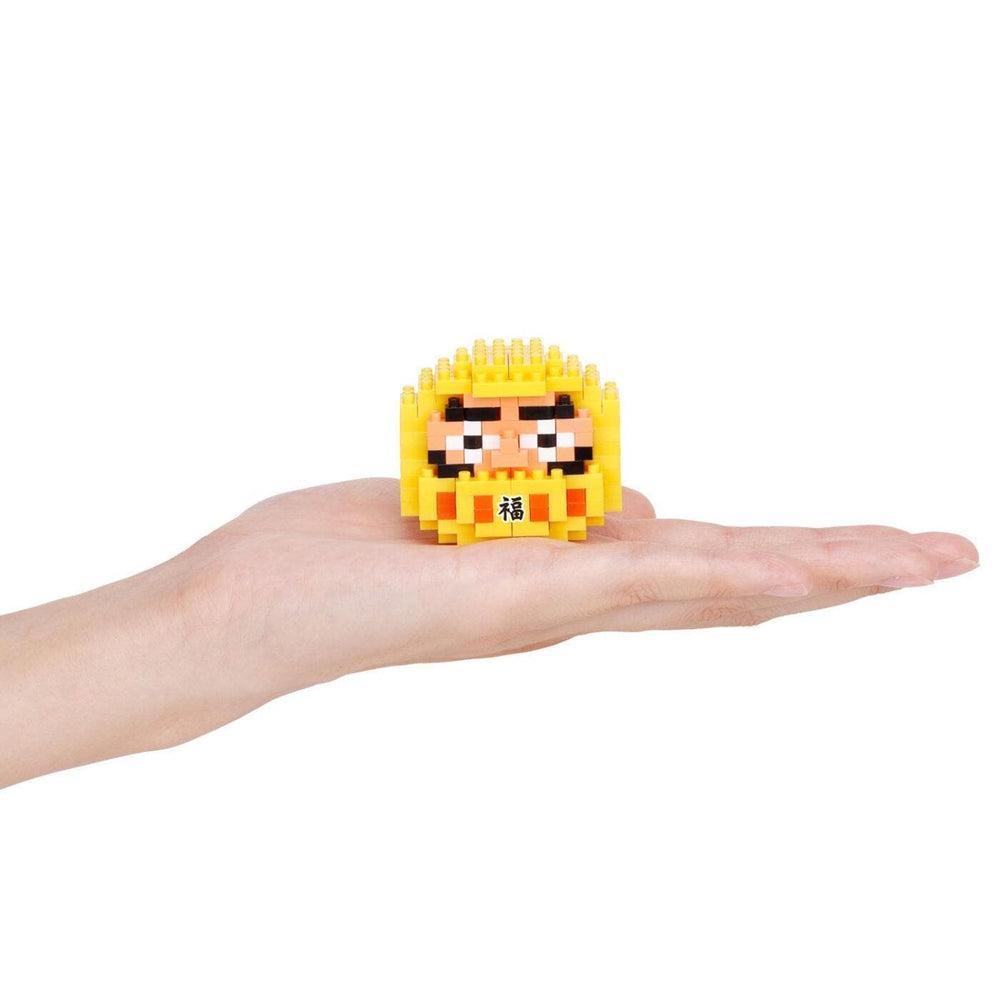 A hand holding a small yellow, pixelated character resembling a face or a character from a video game.