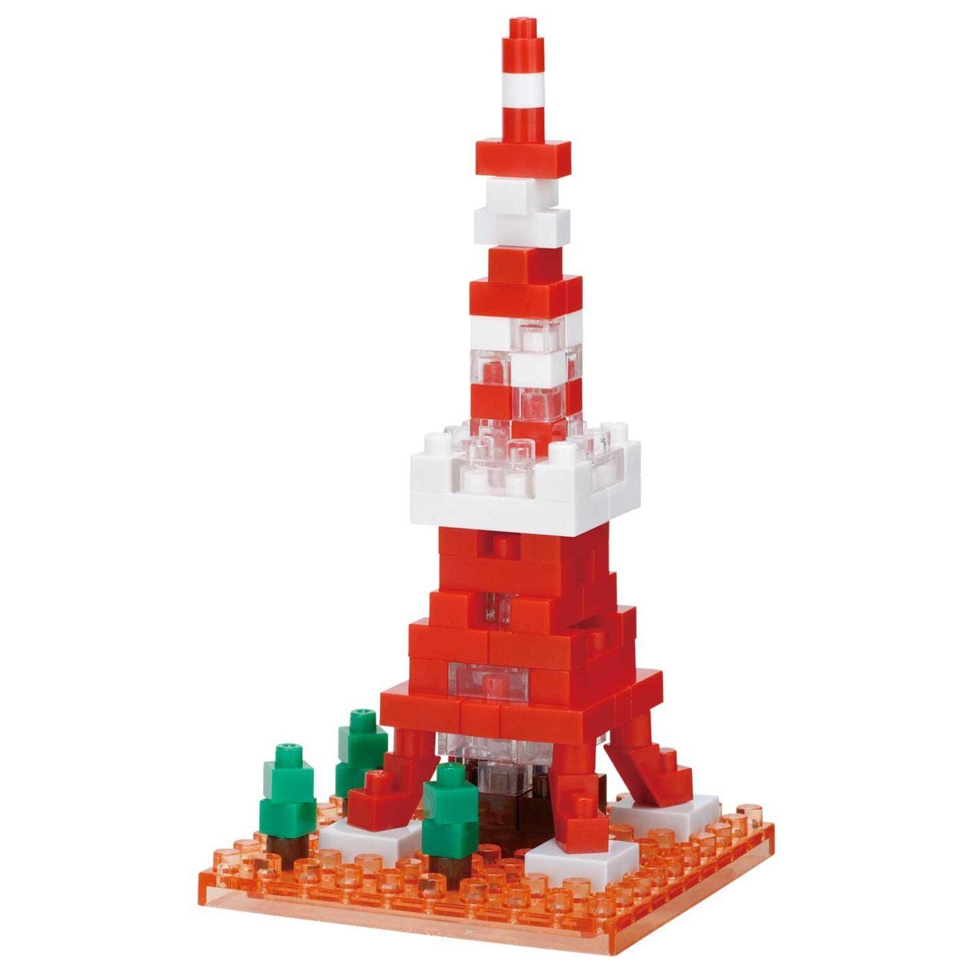 A red and white Lego tower made of small Lego bricks, with a few green Lego trees in the foreground.