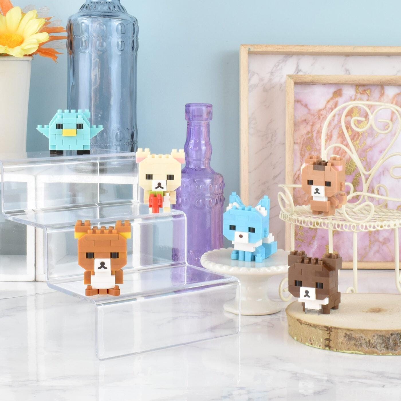 a collection of small, colorful, and whimsical figurines or toys, including a bird, a bear, a cat, and a dog, arranged on a marble surface. There are also some decorative elements such as a vase, a bottle, and a picture frame in the background.