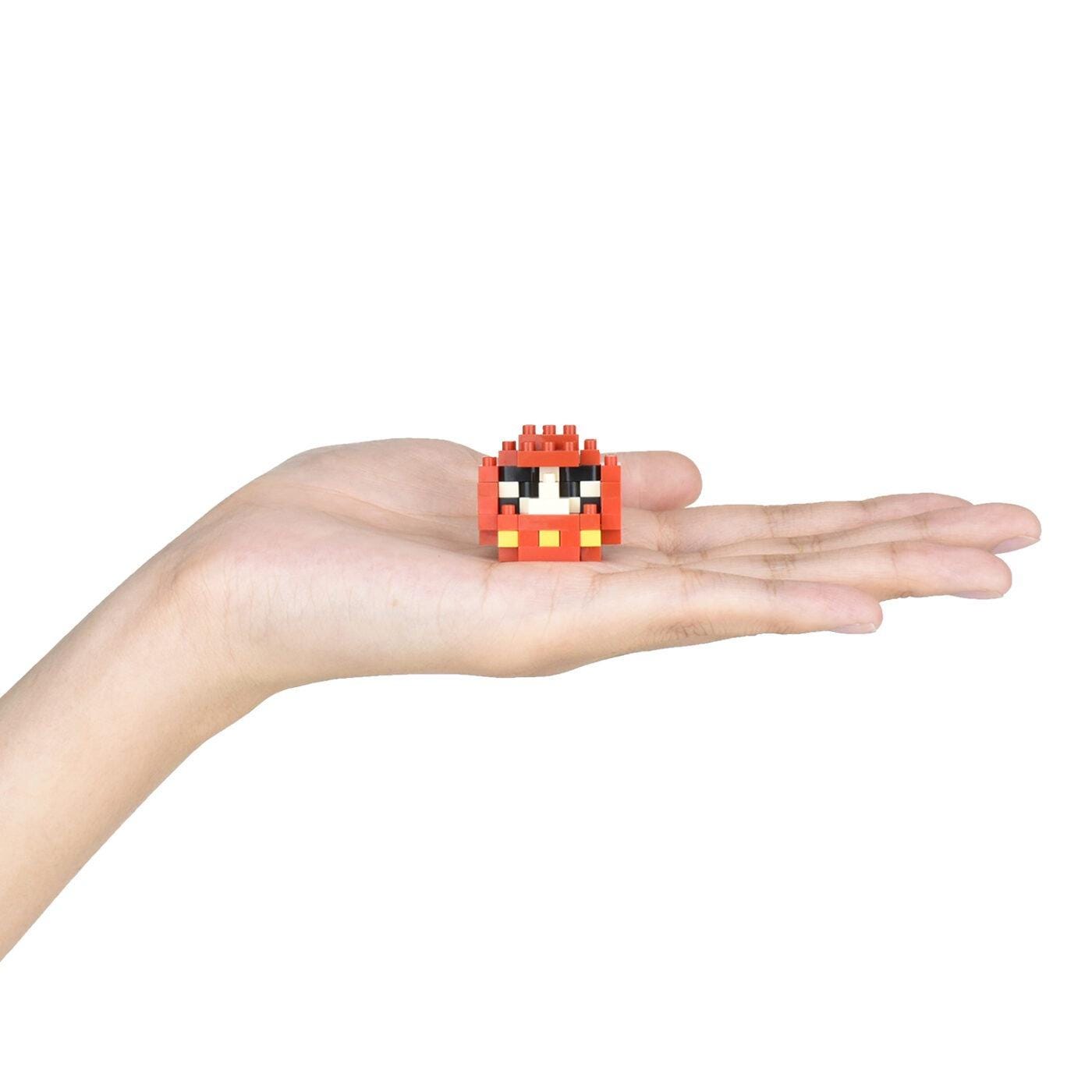 A hand holding a small red and black pixelated character.