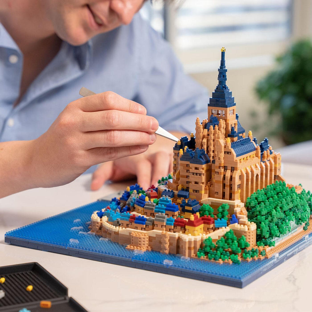 A person is carefully crafting a detailed model of a castle using small, colorful building blocks.
