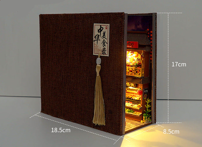 Miniature book nook kit with dark fabric-textured cover and tassel, open side showing lit interior