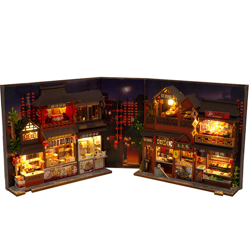 Miniature book nook kit open flat, with two rows of lit food stalls and hanging lantern decorations