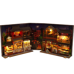 Miniature book nook kit open flat, with two rows of lit food stalls and hanging lantern decorations